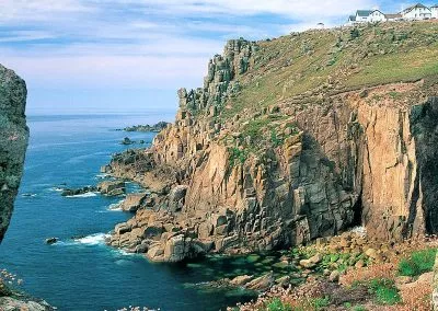 Scenic cliffside view of rugged coastline with blue ocean and clear skies, featuring rustic buildings atop the cliffs.