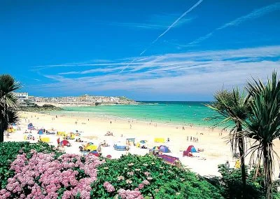 Sunny beach scene with colorful umbrellas, lush greenery, and vibrant flowers under a bright blue sky. Perfect summer getaway.
