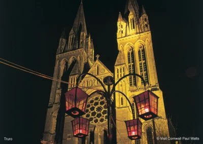 Gothic cathedral illuminated at night with decorative lanterns in the foreground, showcasing intricate architectural details and a vibrant atmosphere.