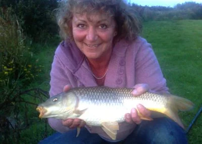 Woman smiling while holding a large fish outdoors, showcasing her successful catch during a fishing trip.