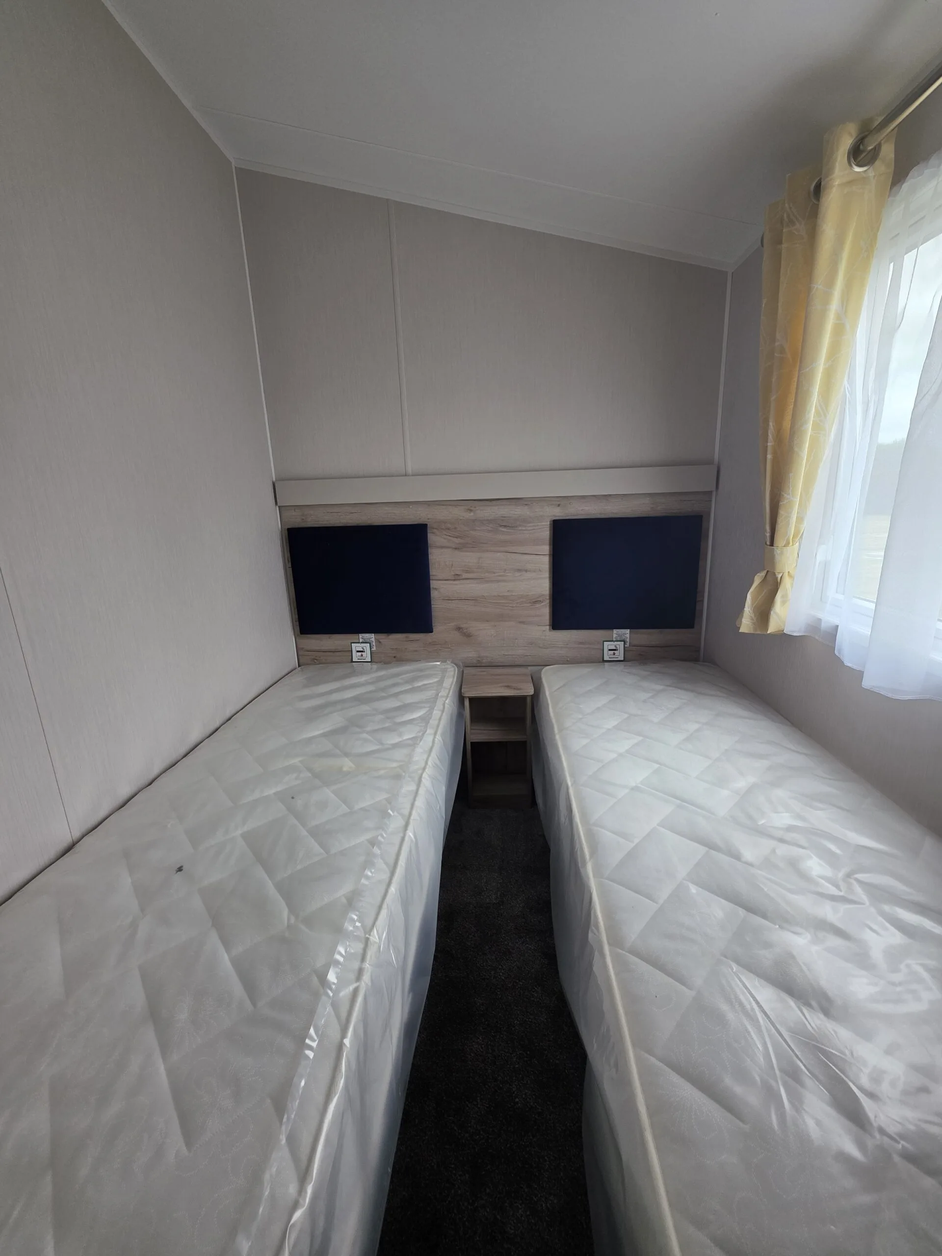 Twin beds in a caravan bedroom with blue headboards and yellow curtains