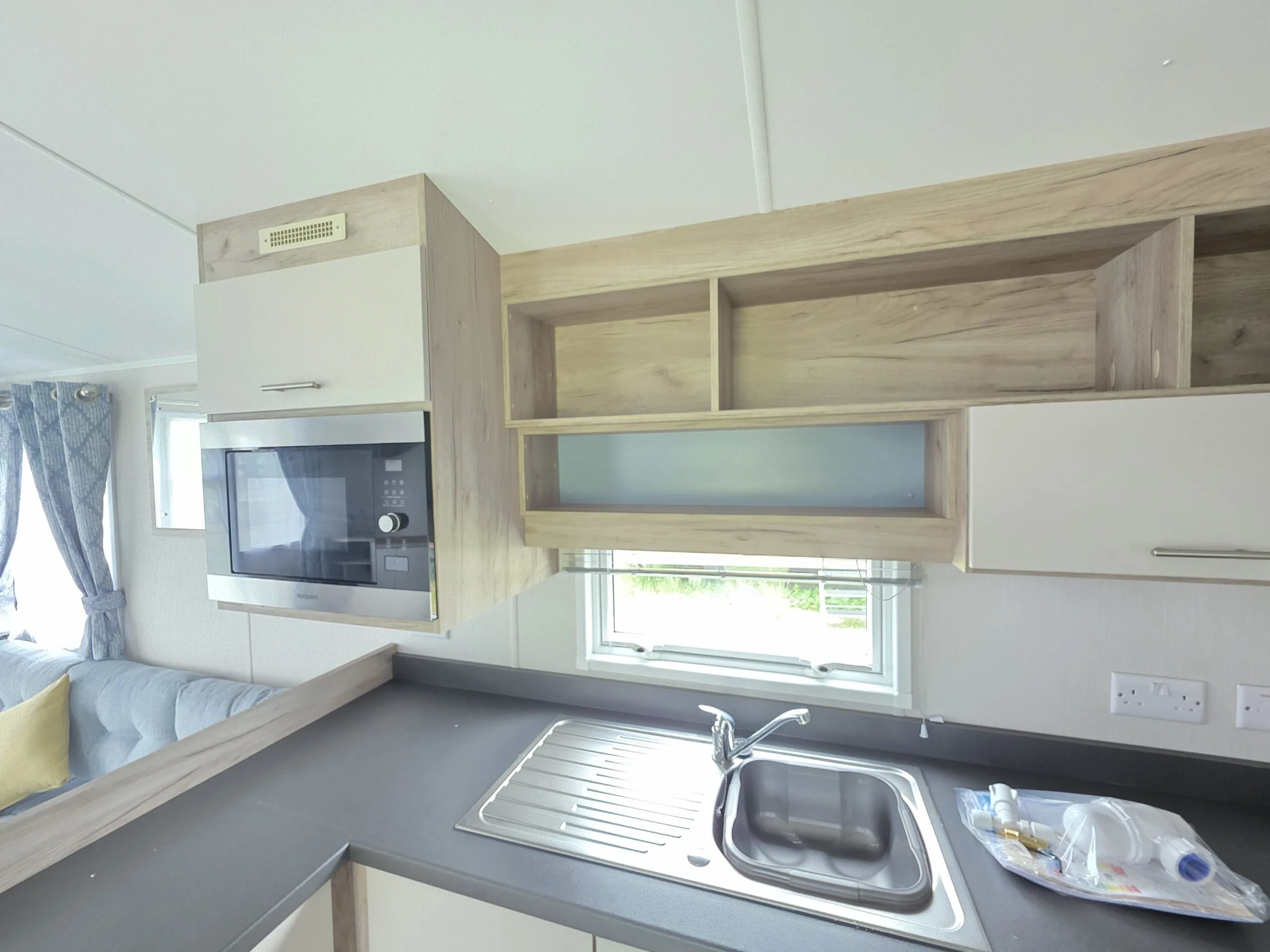 Modern caravan kitchen with sink, microwave, and light wood cabinets.